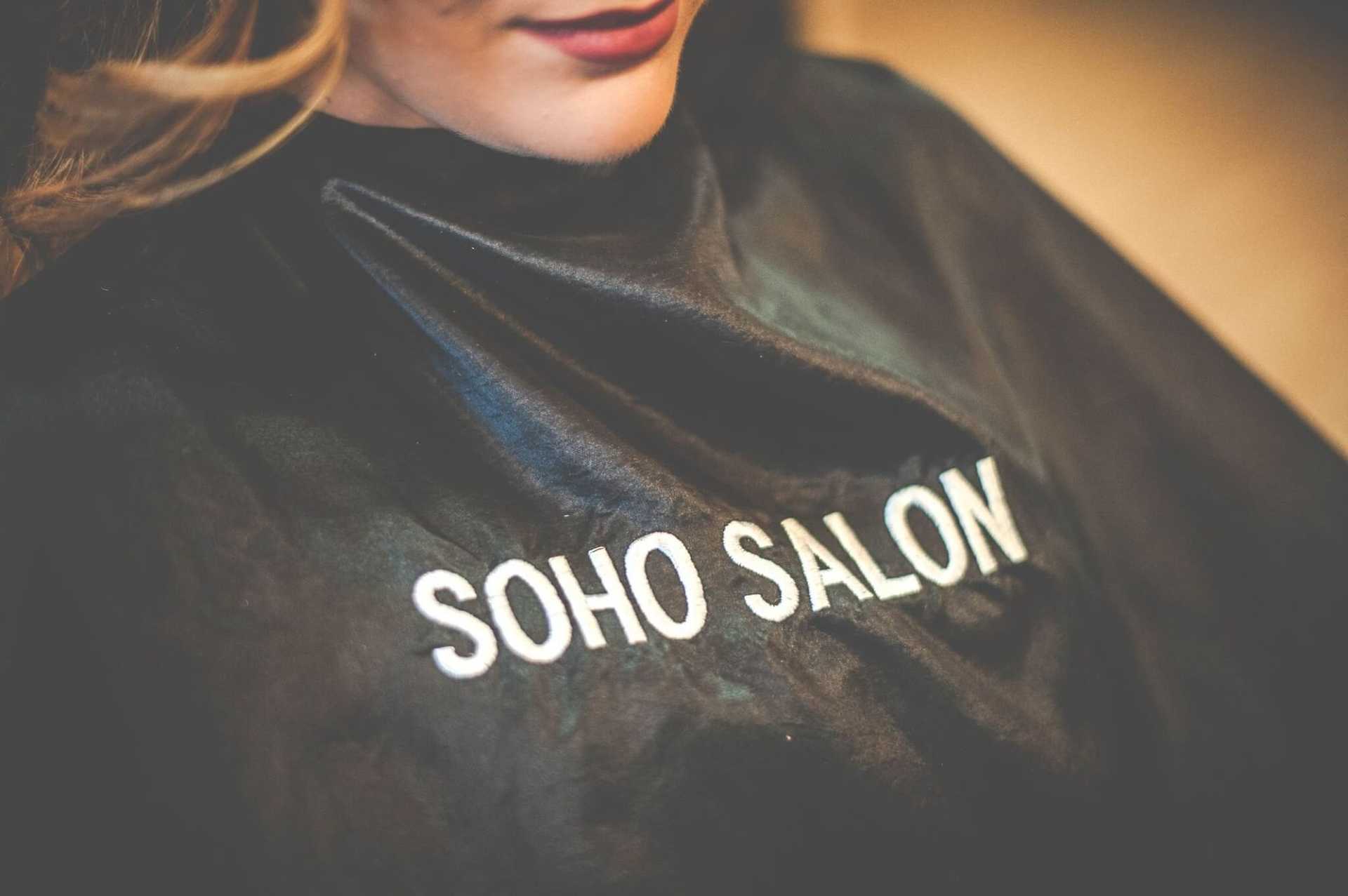Person wearing a salon cape embroidered with "Soho Salon.